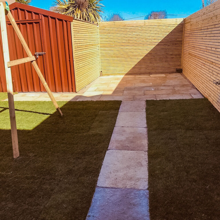 Paving through lawn to fencing enclosing corner patio
